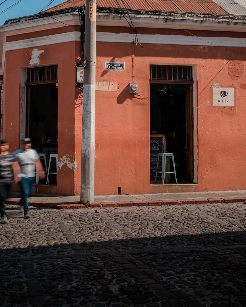 Fachada naranja de Café Raíz en una esquina con calle empedrada en Antigua Guatemala
